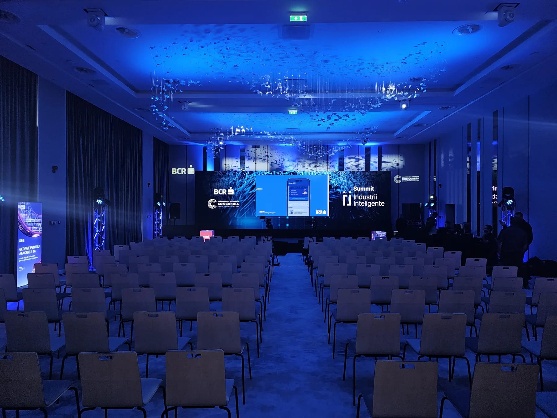 Smart Industries Summit stage in Cluj-Napoca with a wide LED screen, blue lighting and audience seating.