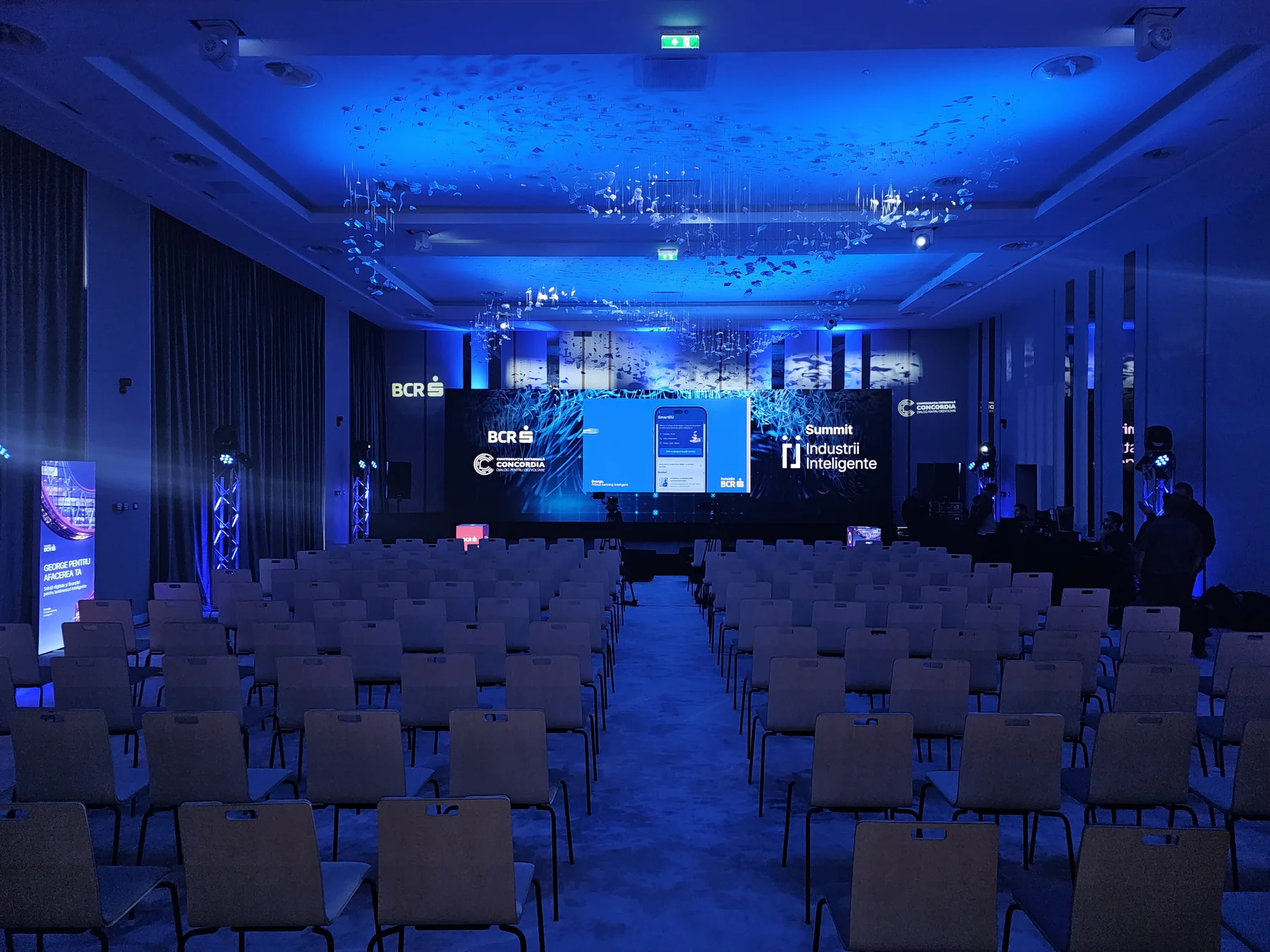 Smart Industries Summit stage in Cluj-Napoca with a wide LED screen, blue lighting and audience seating.