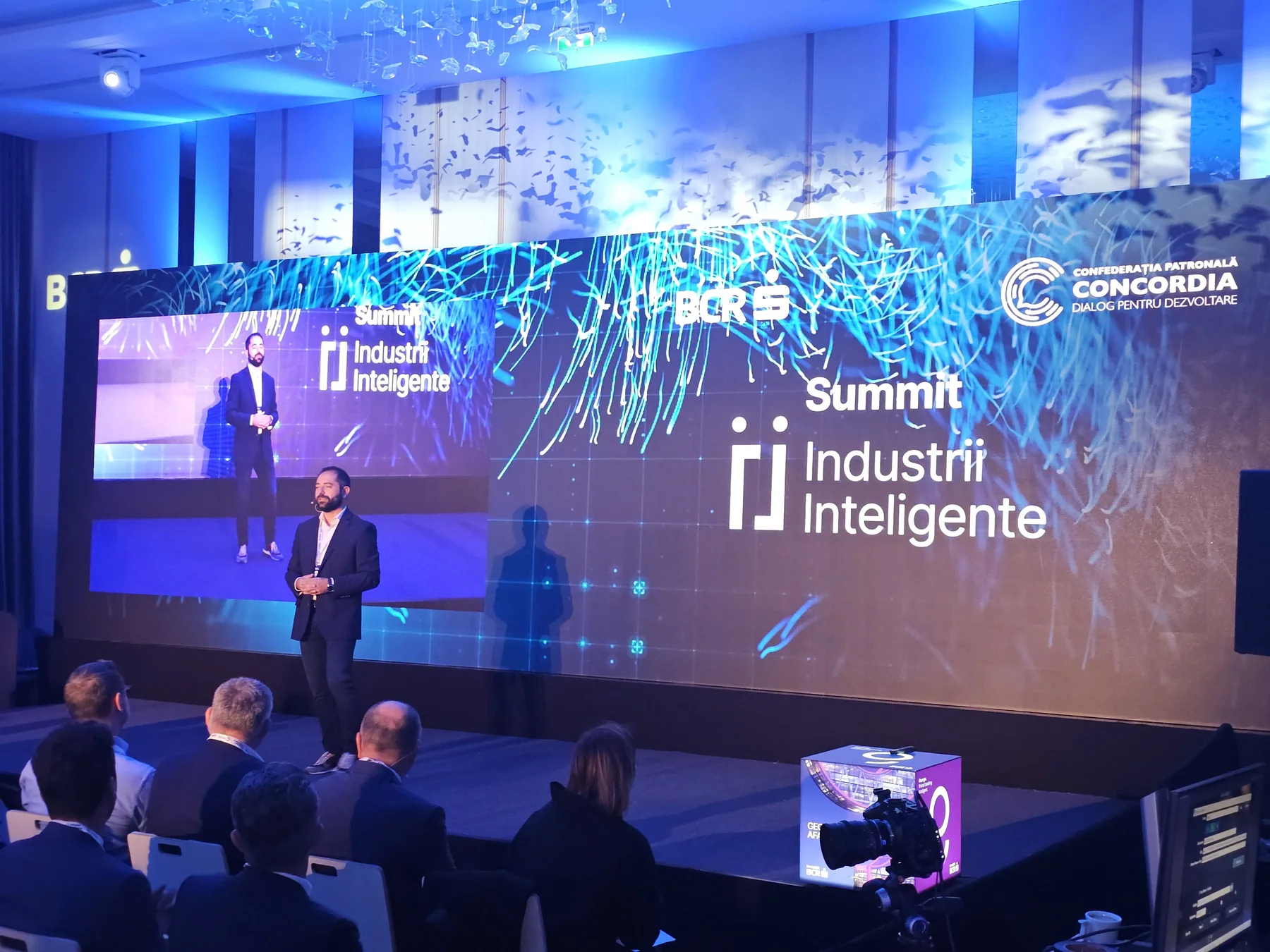 Speaker on the Smart Industries Summit stage with LED content and event lighting in Cluj-Napoca.