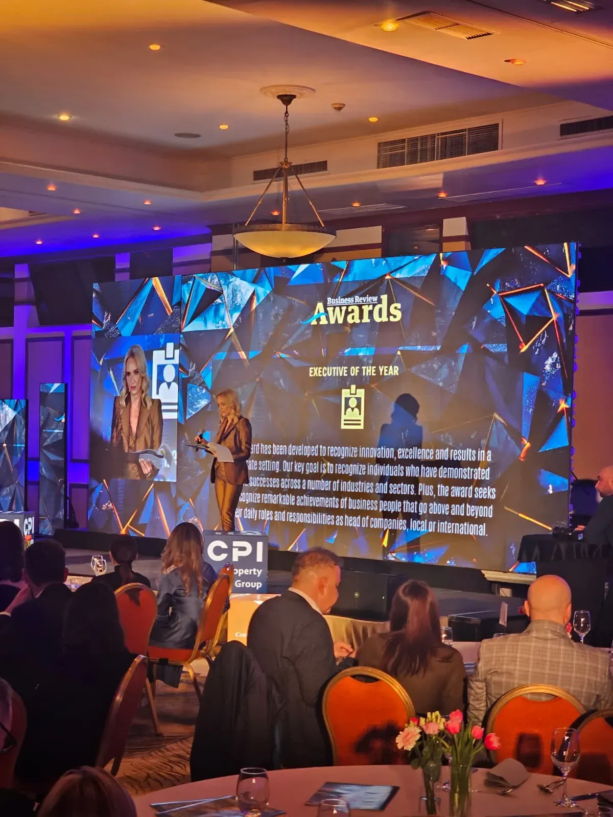 Conference guests facing the LED wall and digital poster displays at the Business Review event in Hotel Caro.