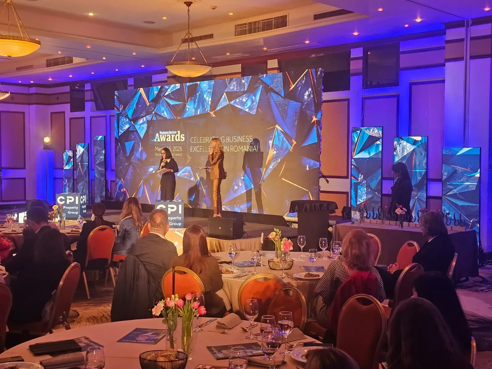 Business Review conference stage with a central LED wall and vertical digital posters at Hotel Caro in Bucharest.