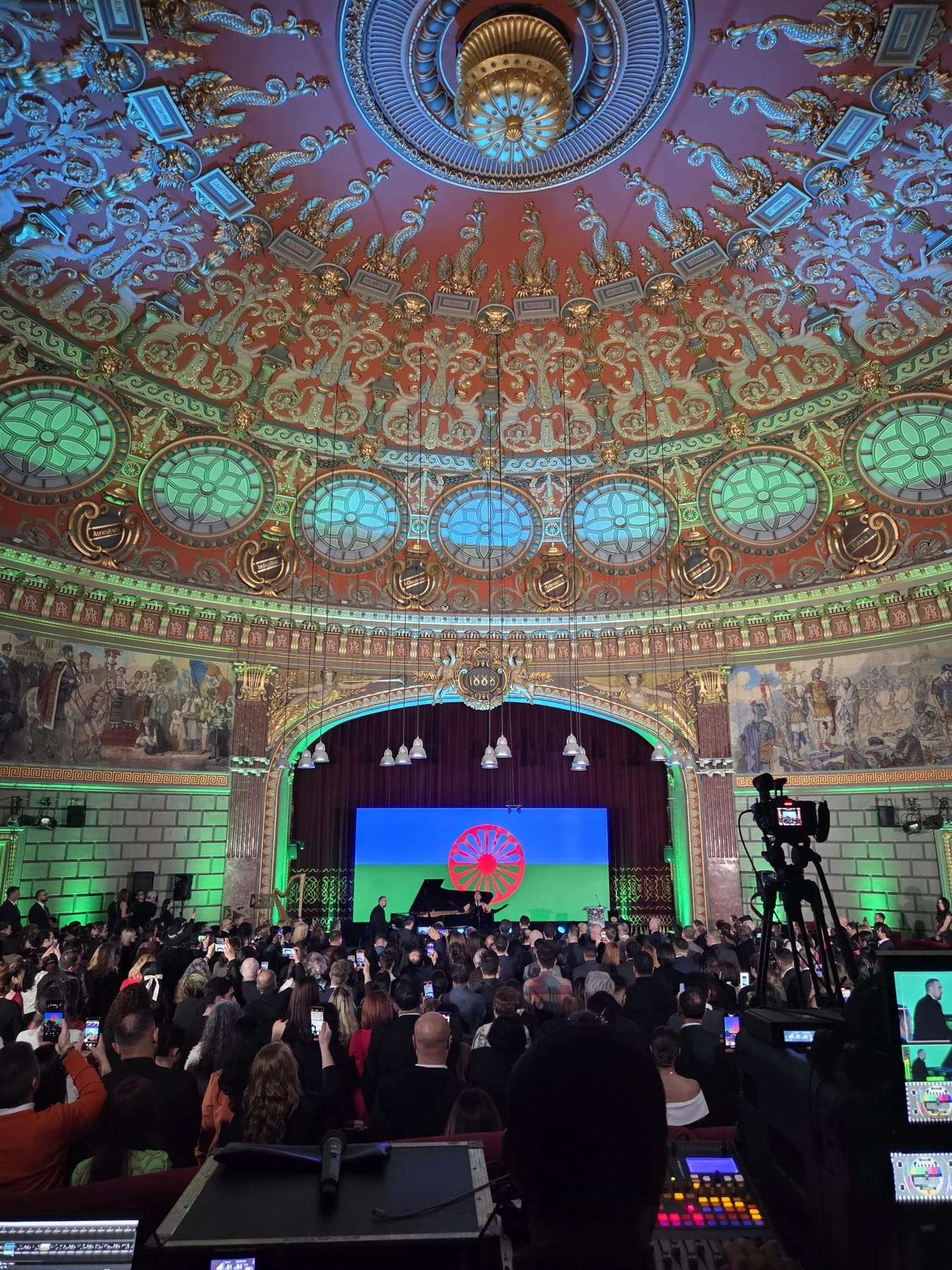 Audience and illuminated stage inside the Romanian Athenaeum during the European Roma Institute event.