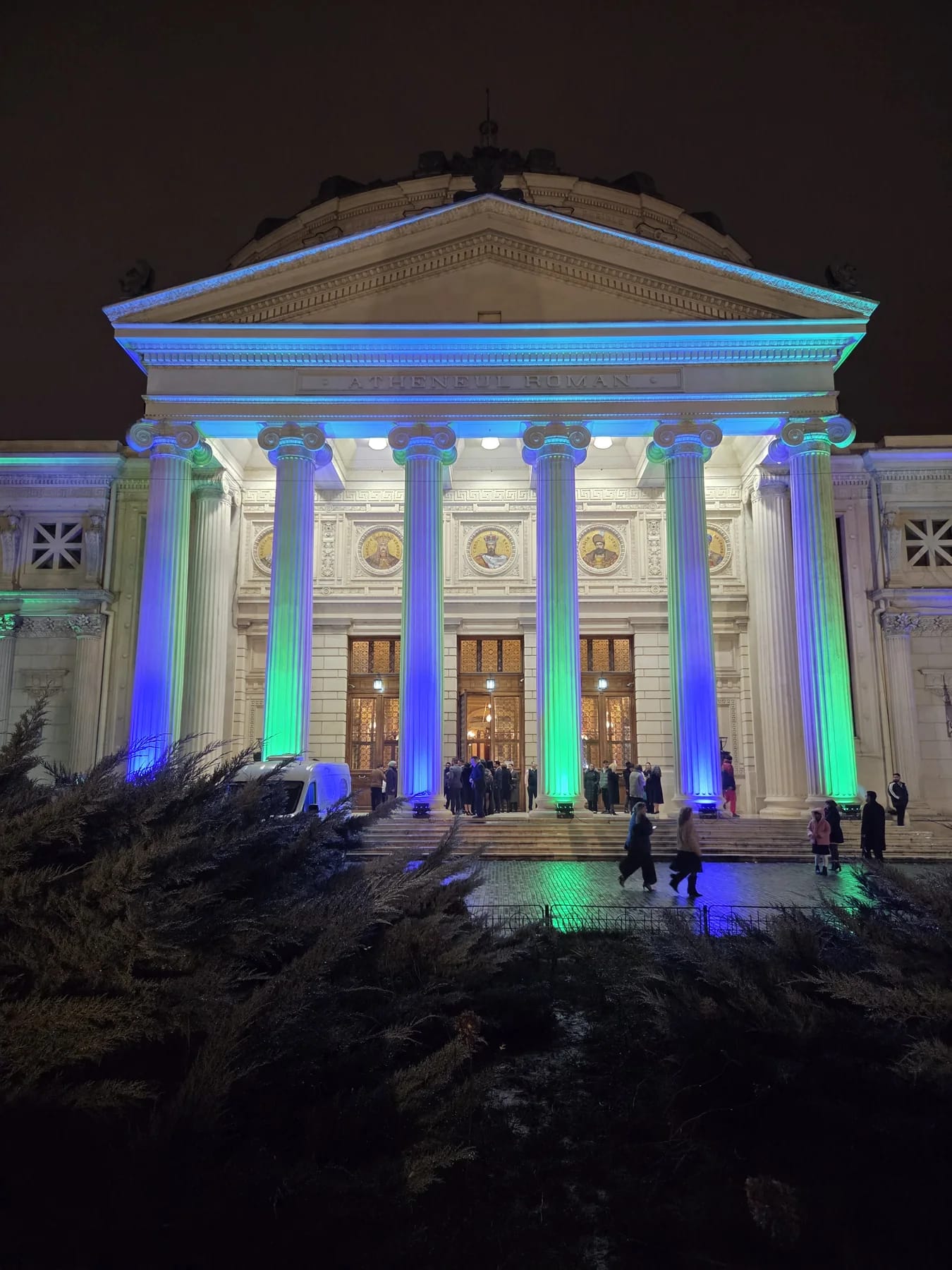 Front façade of the Romanian Athenaeum illuminated in blue and green for the European Roma Institute event.