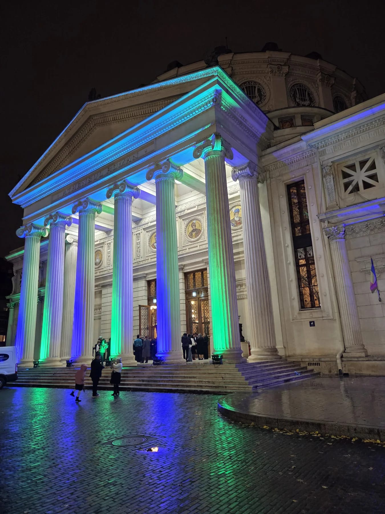 Romanian Athenaeum exterior illuminated in blue and green during the European Roma Institute event in Bucharest.
