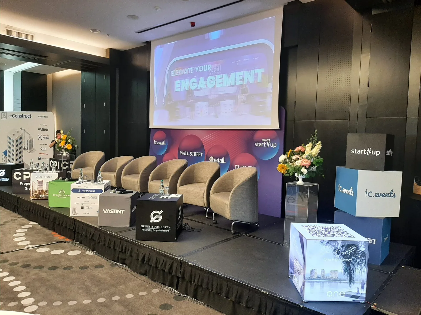 Reconstruct conference stage at Sheraton Bucharest with a presentation screen, panel seating and branded event cubes.
