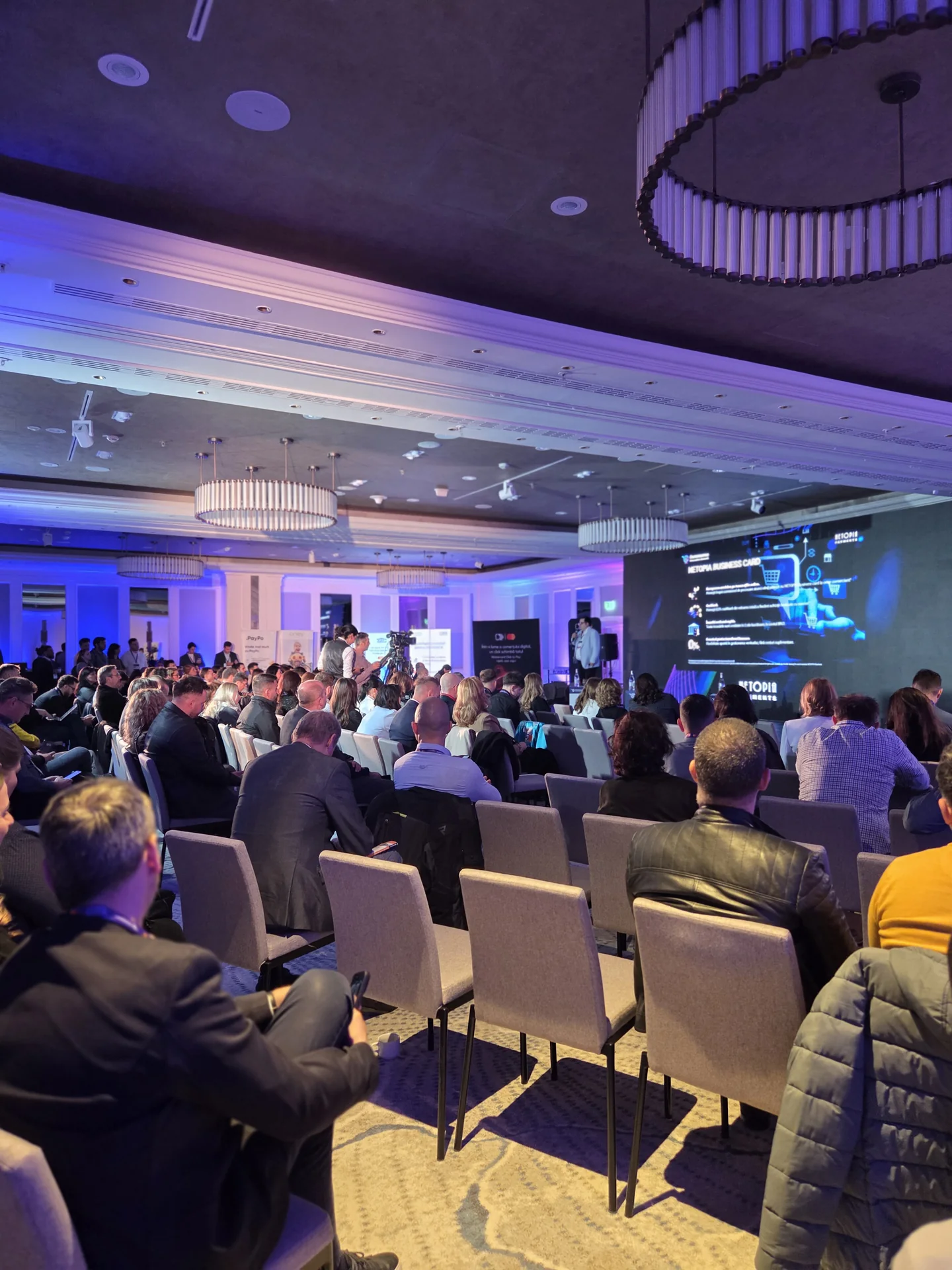 Audience facing the Netopia conference stage and LED screen at Marriott Bucharest.